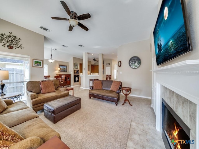 living area featuring a tile fireplace, light carpet, baseboards, visible vents, and ceiling fan