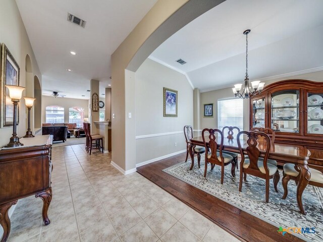 dining area with light tile patterned flooring, vaulted ceiling, crown molding, visible vents, and arched walkways