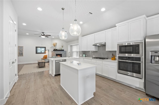 532 Elm Green St, Hutto, TX 78634 - kitchen featuring appliances with stainless steel finishes, under cabinet range hood, a center island, light countertops, and a tile fireplace