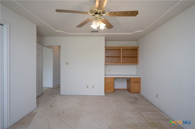 unfurnished office with light colored carpet, built in desk, and ceiling fan