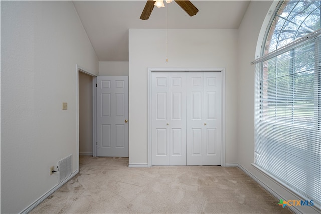 unfurnished bedroom featuring ceiling fan, light colored carpet, a closet, and lofted ceiling