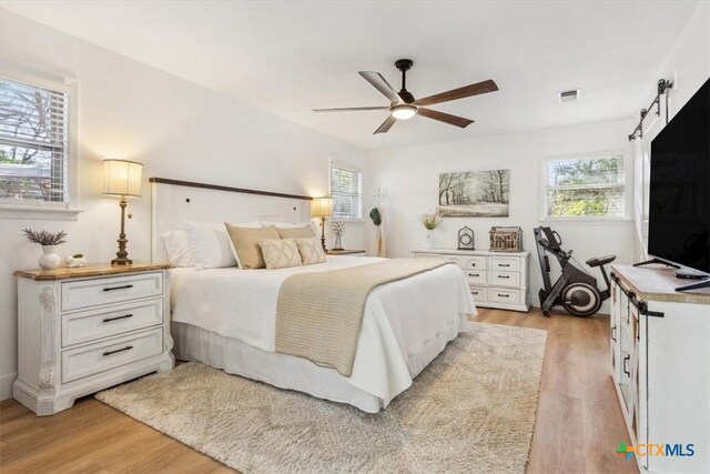 bedroom with a barn door, visible vents, light wood-style floors, and a ceiling fan