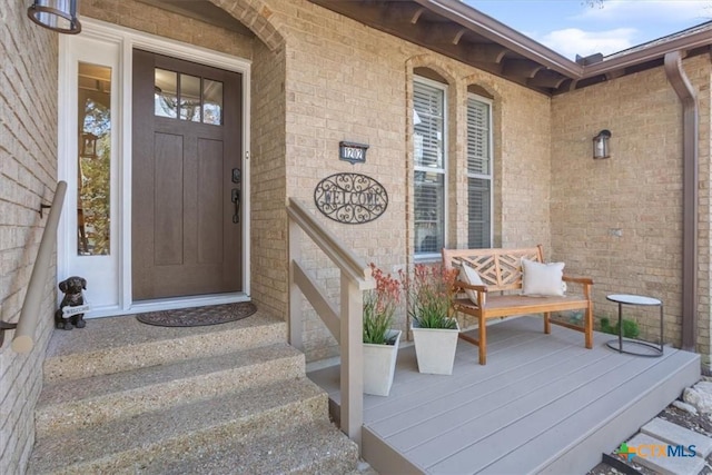 doorway to property with a porch and brick siding