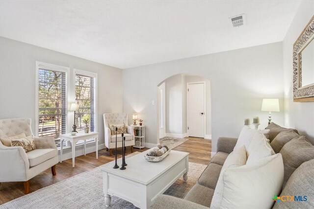 living room with wood finished floors, arched walkways, baseboards, and visible vents
