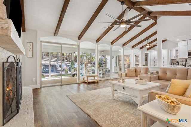 living area with a warm lit fireplace, high vaulted ceiling, beamed ceiling, a ceiling fan, and light wood-style floors