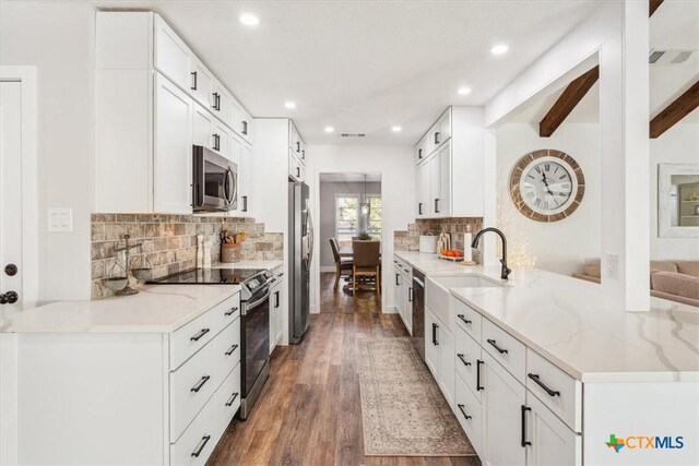 kitchen featuring beam ceiling, wood finished floors, a peninsula, stainless steel appliances, and visible vents