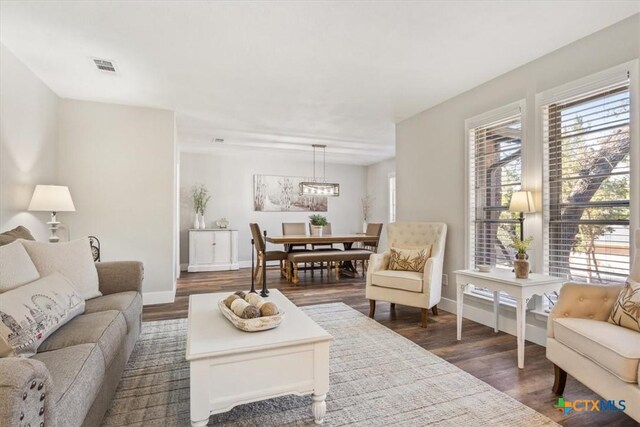 living area with baseboards, dark wood-style flooring, visible vents, and an inviting chandelier