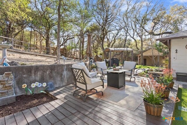 wooden deck with an outdoor fire pit, an outbuilding, and fence