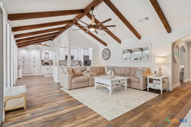 living area with light wood-style flooring, high vaulted ceiling, arched walkways, visible vents, and a ceiling fan