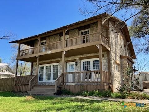 view of front facade with stone siding, a balcony, a porch, and a front yard
