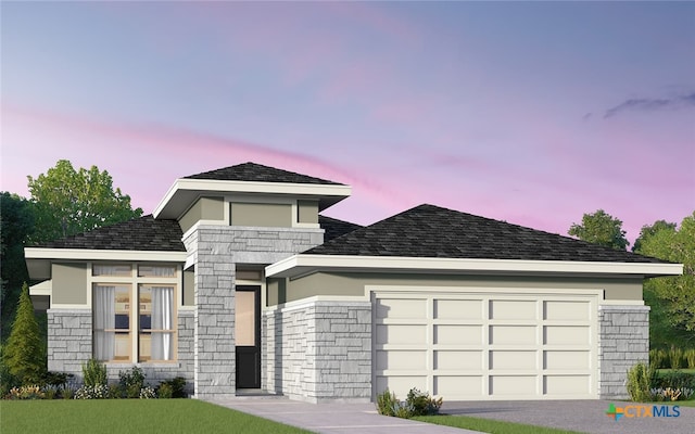 prairie-style house featuring stone siding, roof with shingles, an attached garage, and a lawn