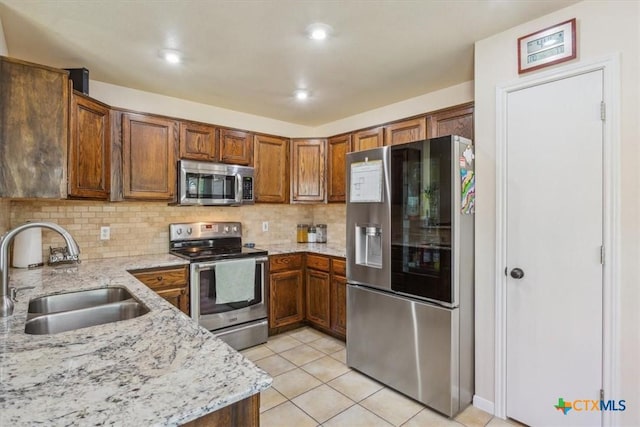 7204 Bluegrass Ct, Temple, TX 76502 - kitchen with appliances with stainless steel finishes, a sink, brown cabinetry, backsplash, and light stone countertops