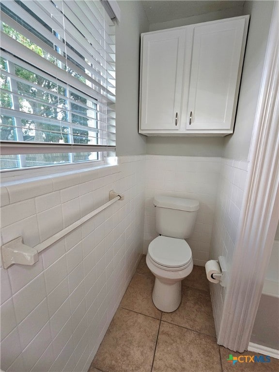 bathroom with a wealth of natural light, tile patterned floors, toilet, and tile walls