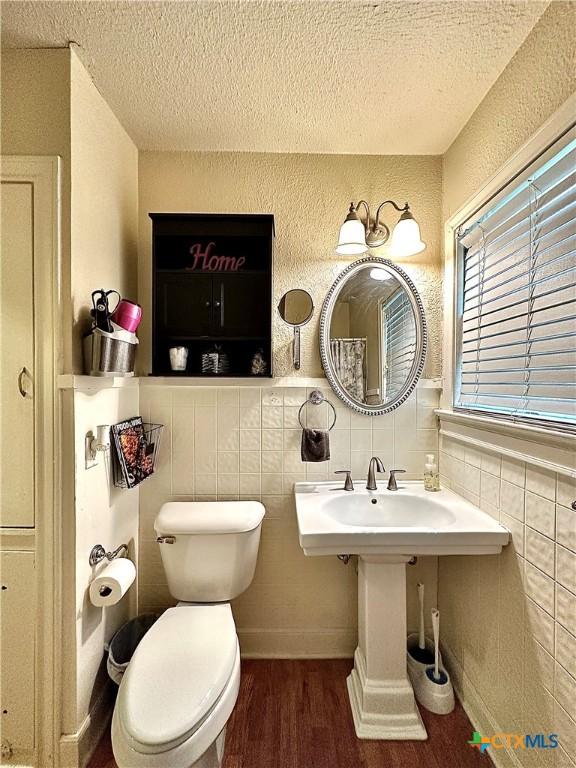 bathroom with toilet, tile walls, a textured ceiling, and wood finished floors