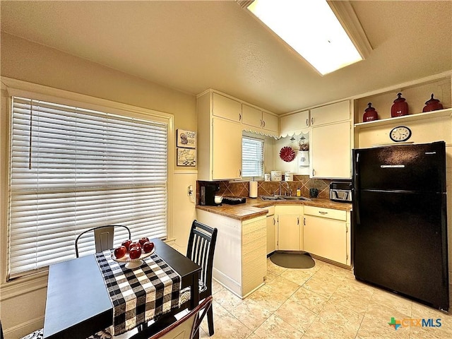 kitchen featuring open shelves, tasteful backsplash, a sink, and freestanding refrigerator