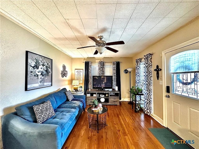 living room featuring ornamental molding, ceiling fan, baseboards, and wood finished floors