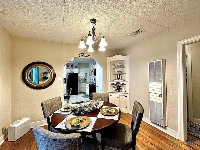 dining space featuring light wood-style floors, visible vents, arched walkways, and an inviting chandelier