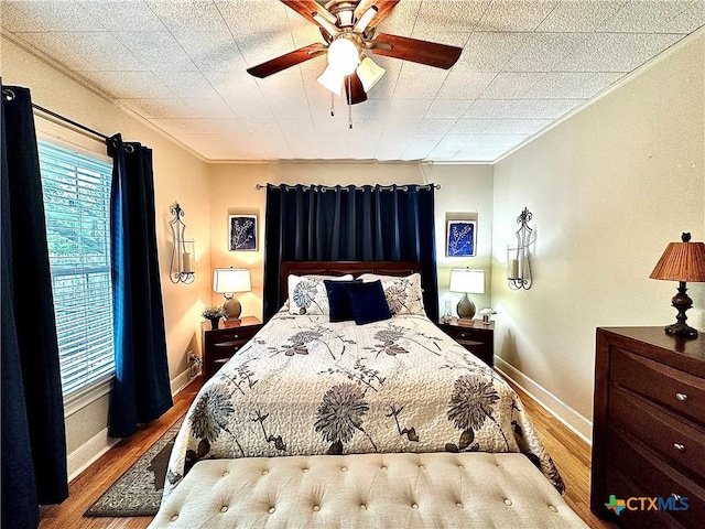 bedroom featuring a ceiling fan, crown molding, baseboards, and wood finished floors