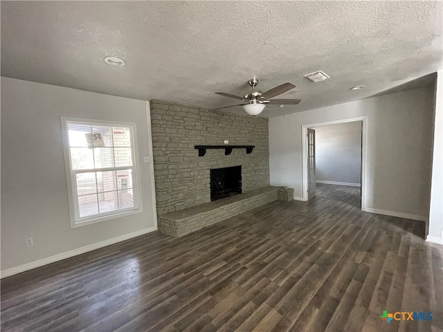 unfurnished living room with a textured ceiling, a stone fireplace, ceiling fan, and dark wood-type flooring