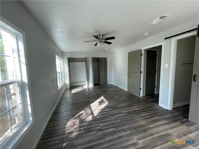 unfurnished bedroom featuring a textured ceiling, a barn door, dark hardwood / wood-style floors, and ceiling fan