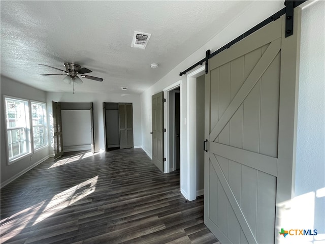 hallway featuring a barn door, dark hardwood / wood-style flooring, and a textured ceiling