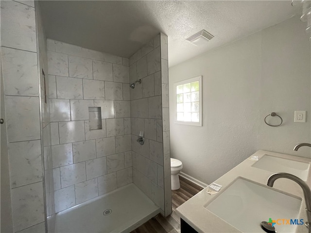 bathroom with vanity, hardwood / wood-style flooring, toilet, a textured ceiling, and a tile shower