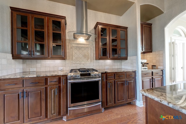 kitchen featuring tasteful backsplash, light stone countertops, light hardwood / wood-style floors, stainless steel range with gas stovetop, and wall chimney exhaust hood