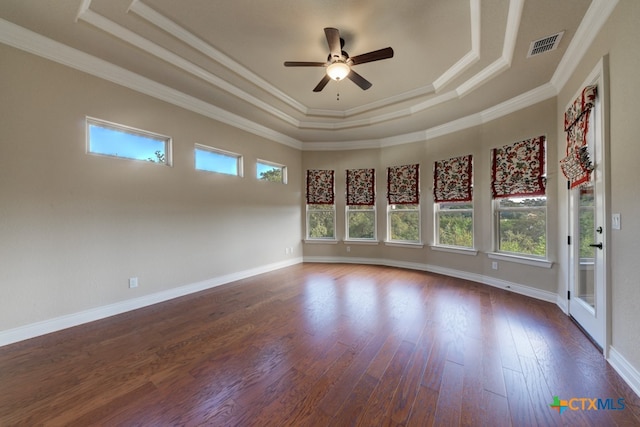 empty room featuring a healthy amount of sunlight, a raised ceiling, dark hardwood / wood-style flooring, and crown molding