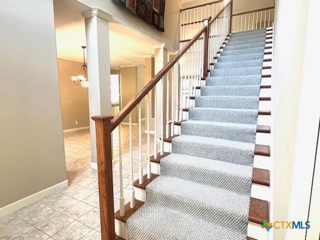staircase with a chandelier, ornate columns, baseboards, and tile patterned floors
