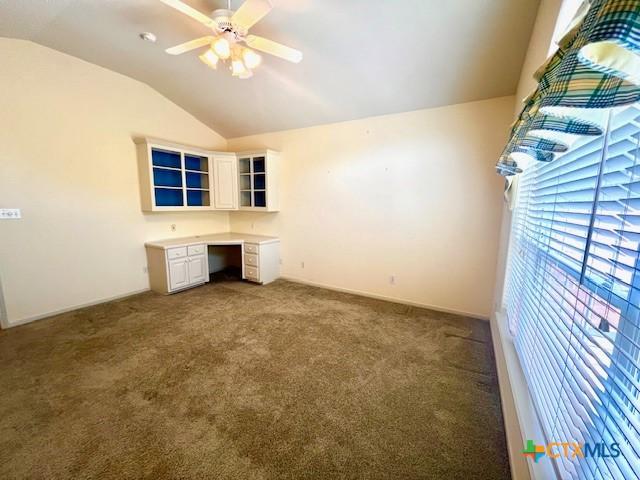 unfurnished bedroom with dark carpet, built in study area, a ceiling fan, and lofted ceiling