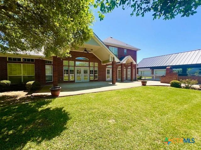 rear view of property featuring a yard, a ceiling fan, a patio, brick siding, and french doors