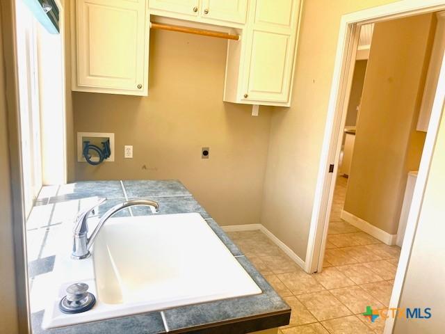 clothes washing area featuring electric dryer hookup, light tile patterned flooring, hookup for a washing machine, cabinet space, and a sink