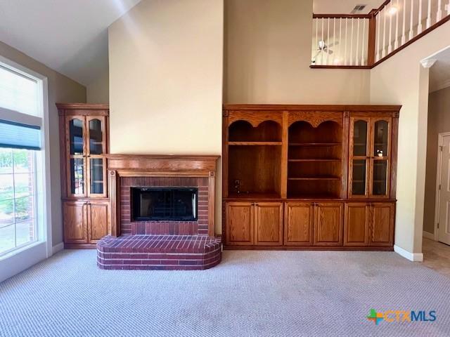 unfurnished living room featuring light carpet, high vaulted ceiling, a fireplace, and baseboards
