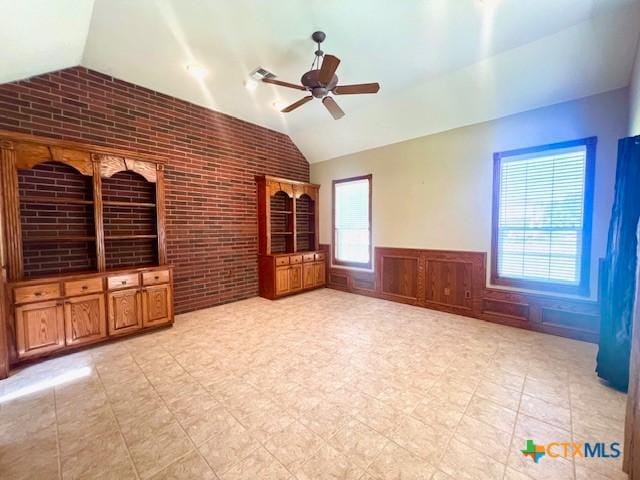 spare room with brick wall, a wainscoted wall, ceiling fan, and vaulted ceiling