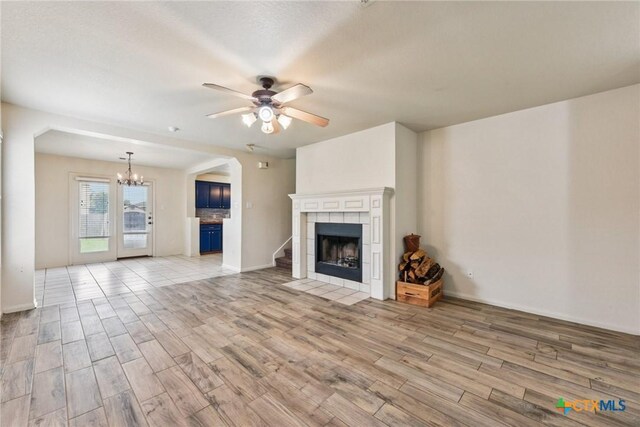 2204 Mikulec Dr, Killeen, TX 76542 - unfurnished living room featuring a chandelier, light wood-style flooring, a ceiling fan, a tiled fireplace, and baseboards