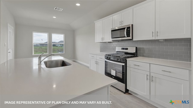 kitchen with light wood-type flooring, stainless steel appliances, sink, a center island with sink, and white cabinetry