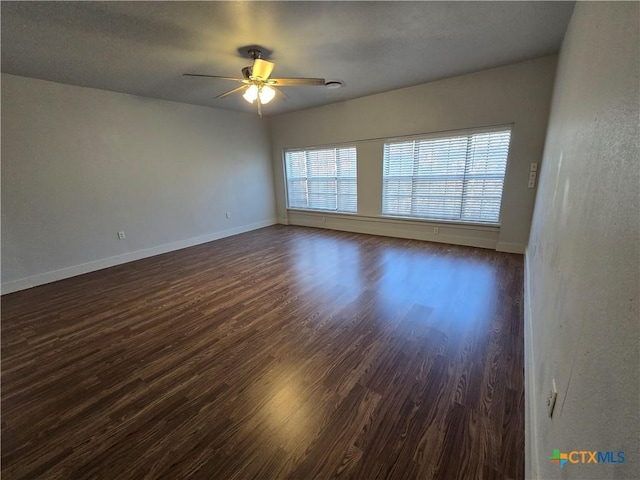 unfurnished room with a ceiling fan, baseboards, and dark wood-type flooring