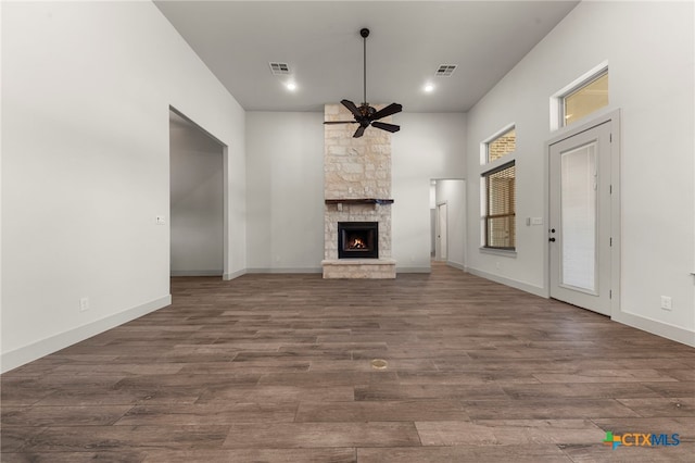 unfurnished living room featuring ceiling fan, dark hardwood / wood-style floors, and a stone fireplace