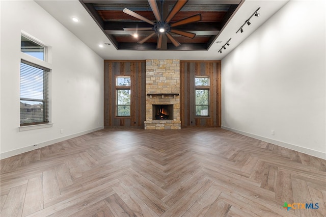 unfurnished living room with ceiling fan, a healthy amount of sunlight, a stone fireplace, and light parquet floors