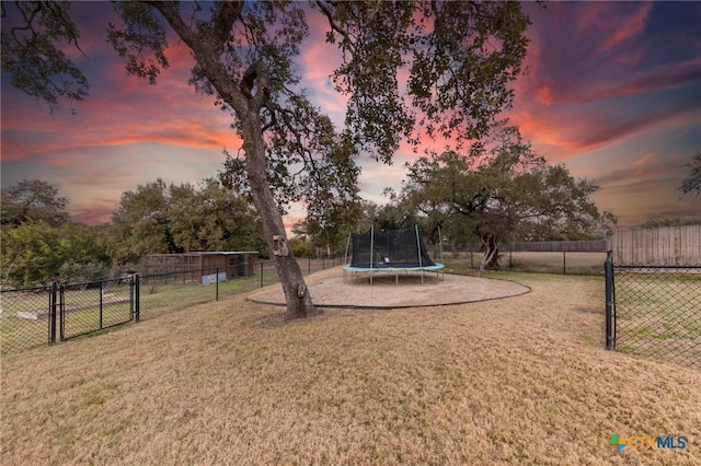 playground at dusk featuring a trampoline and a yard