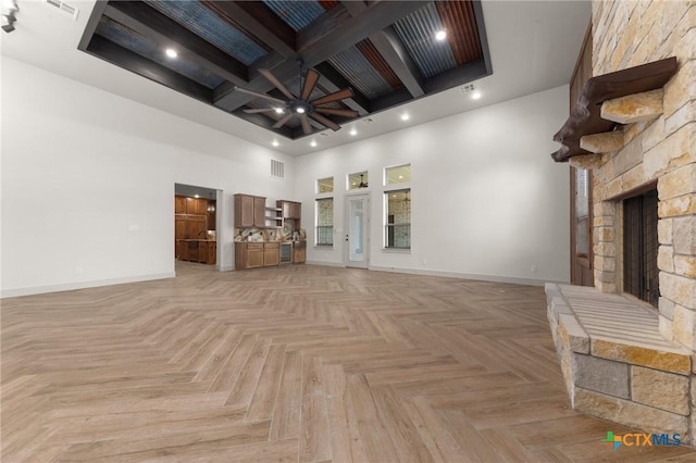 unfurnished living room with coffered ceiling, ceiling fan, a high ceiling, a fireplace, and light parquet flooring