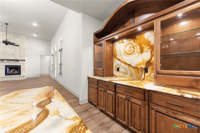 bar with light hardwood / wood-style floors, ceiling fan, a fireplace, light stone countertops, and sink