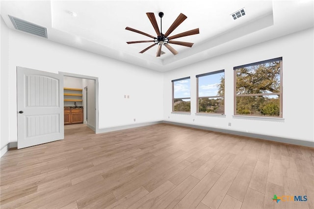 interior space featuring a raised ceiling, ceiling fan, and light hardwood / wood-style floors