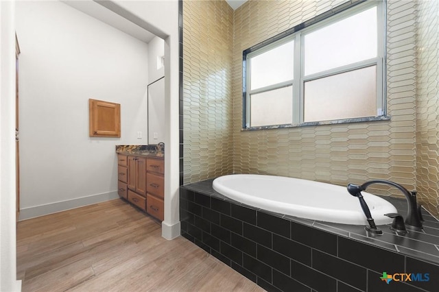 bathroom featuring vanity, wood-type flooring, and a relaxing tiled tub