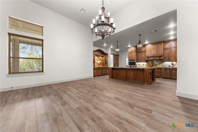 kitchen featuring decorative light fixtures, a center island, stainless steel oven, and light wood-type flooring