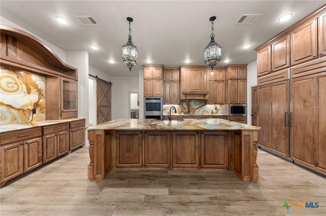 kitchen with hanging light fixtures, a barn door, stainless steel appliances, and a center island with sink