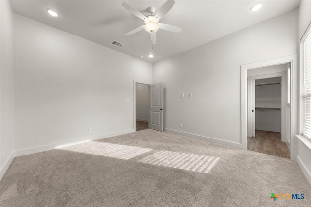 unfurnished bedroom with a spacious closet, multiple windows, a closet, ceiling fan, and light colored carpet