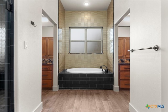 bathroom featuring backsplash, tiled tub, hardwood / wood-style flooring, and vanity