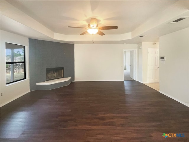 unfurnished living room with dark wood-type flooring, a tray ceiling, and a fireplace