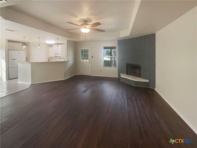 unfurnished living room featuring dark hardwood / wood-style flooring, a raised ceiling, ceiling fan, and a brick fireplace